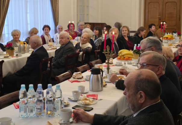 Grupa osób siedzi w eleganckie sali przy zastawionych stołach