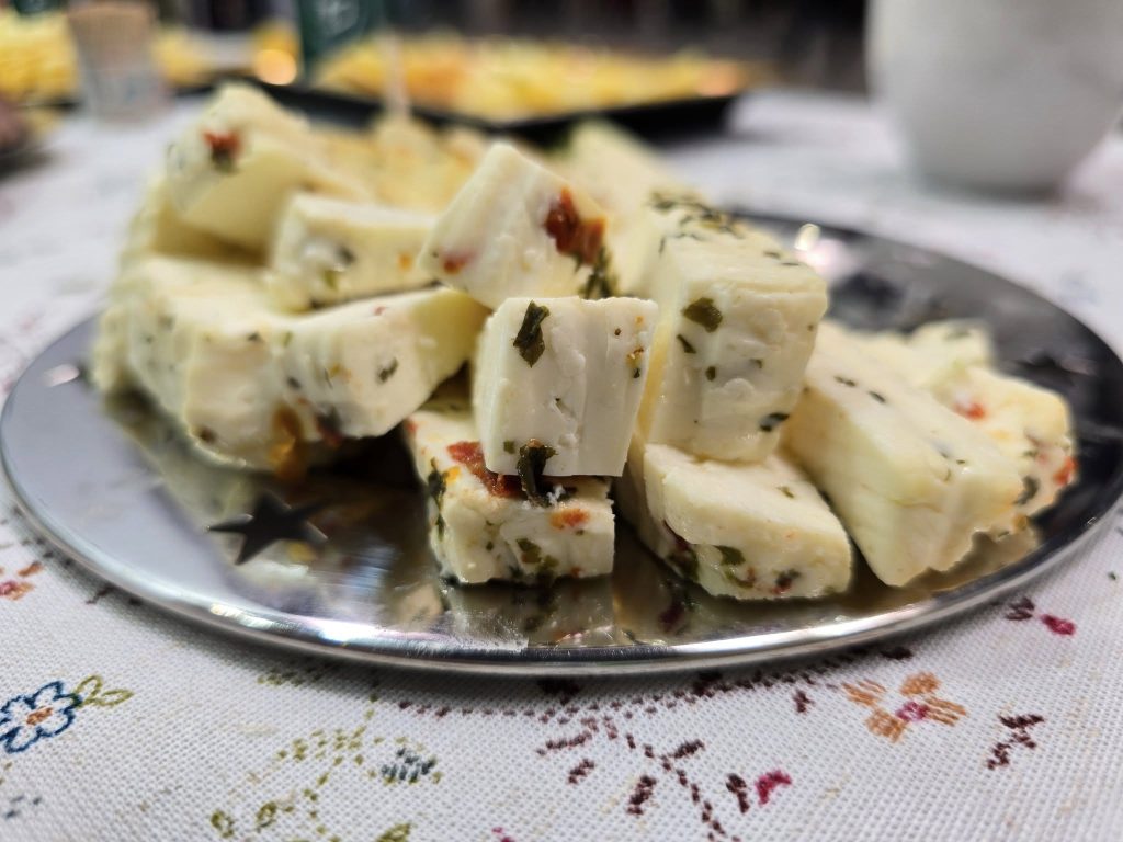 Kawałki białego sera z ziołami i warzywami ułożone na metalowym talerzu, stojącym na ozdobnym obrusie podczas degustacji.