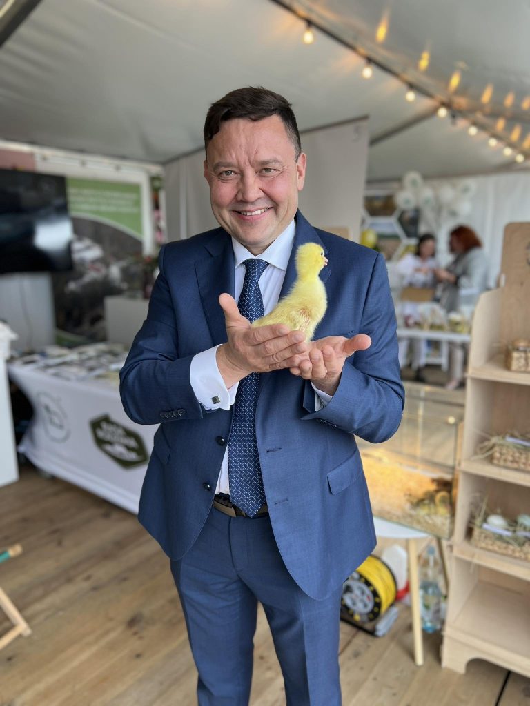 Dyrektor Instytutu Zootechniki z pisklęciem w dłoniach podczas wizyty na stoisku promującym rodzimą hodowlę.