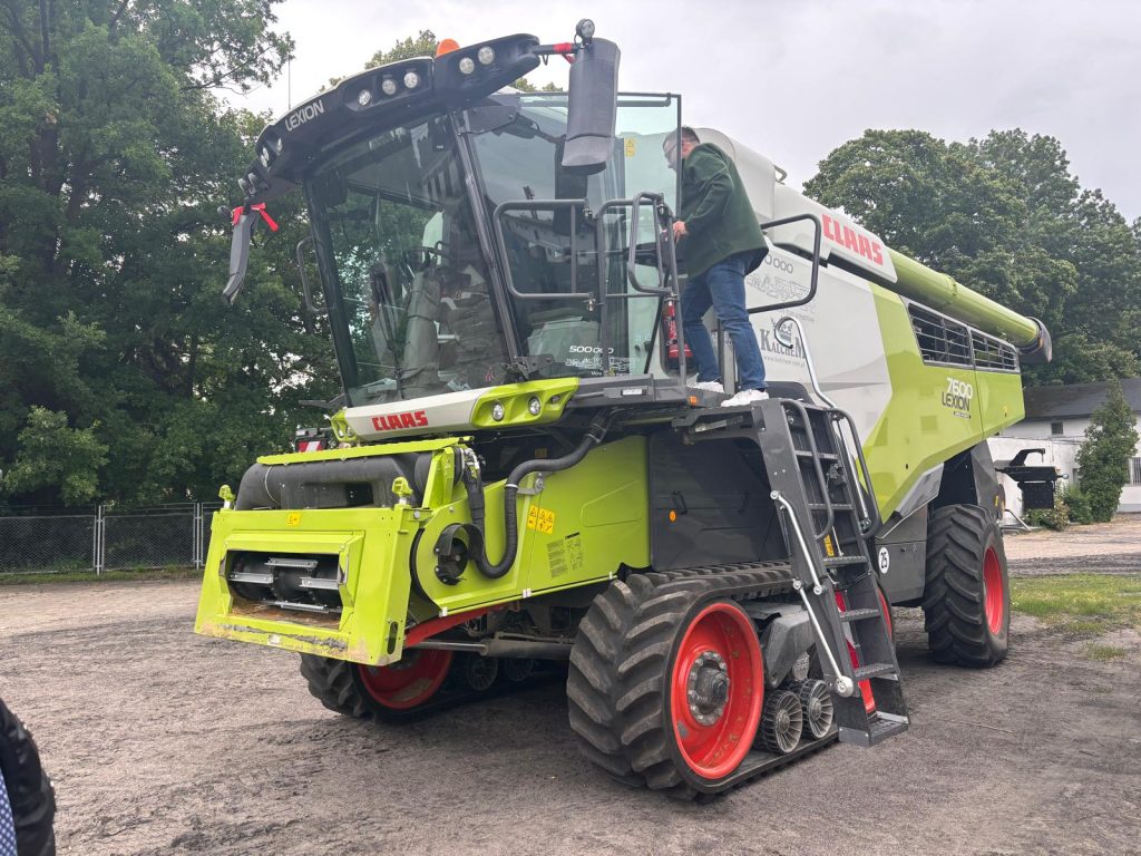 Nowoczesny kombajn Claas Lexion 7600 z osobą wchodzącą do kabiny na terenie gospodarstwa.