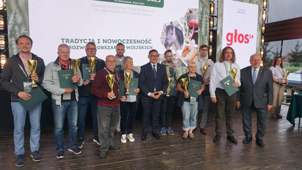 Laureaci konkursu stoją na scenie podczas wydarzenia „Agro Promocja 2025”, trzymając złote puchary i zielone teczki. Pośrodku stoją organizatorzy w garniturach, a w tle widoczny jest ekran z hasłem o tradycji i nowoczesności na obszarach wiejskich.