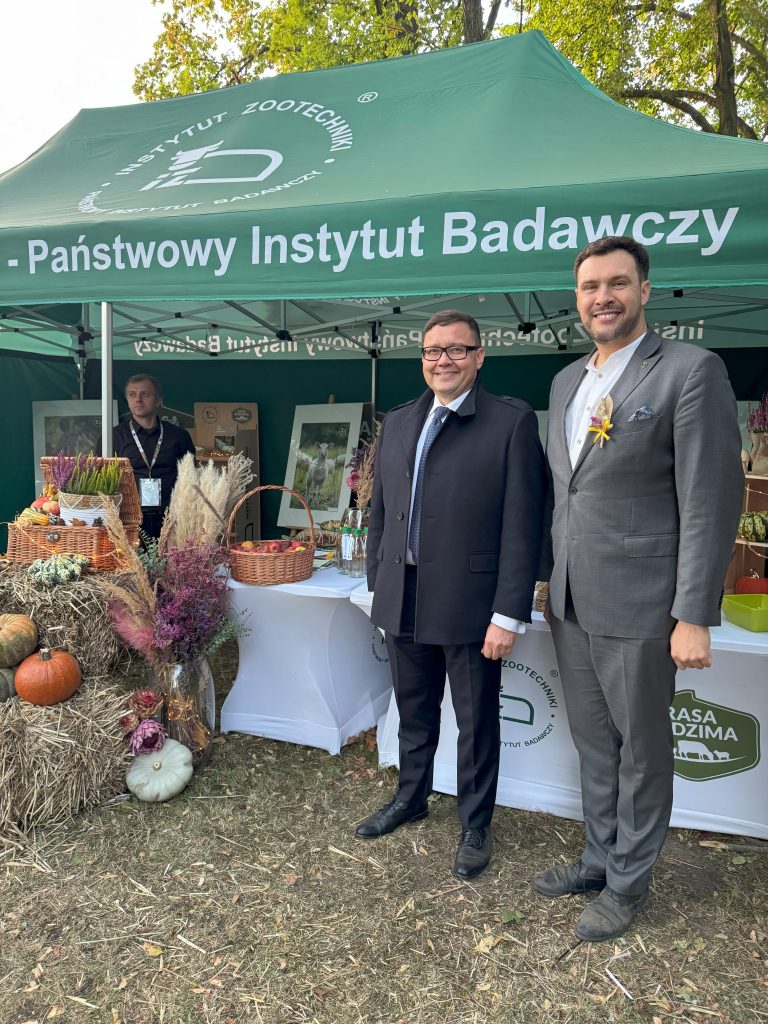 Dwóch mężczyzn stoi przed namiotem wystawowym, pozując do wspólnego zdjęcia.