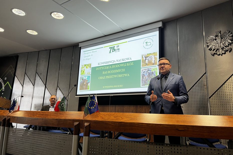 Mężczyzna przemawia na konferencji naukowej o hodowli kóz i ras rodzimych, na ekranie tytuł prezentacji.