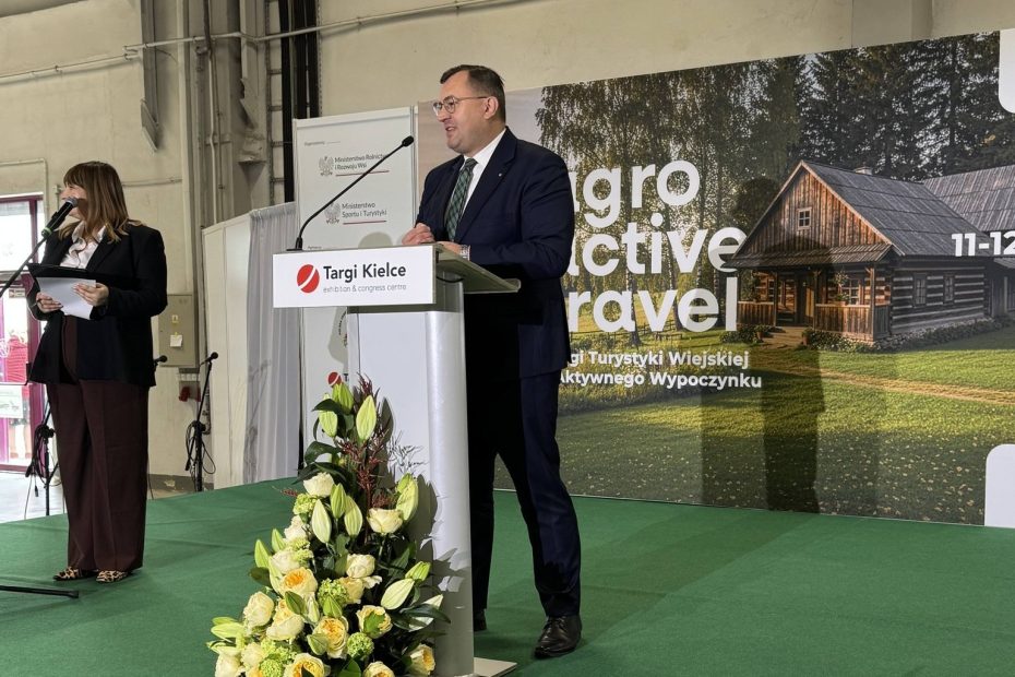 Mężczyzna w garniturze przemawia przy mównicy na wydarzeniu targowym Targi Kielce, obok stoi kobieta z mikrofonem; w tle grafika promująca turystykę wiejską.