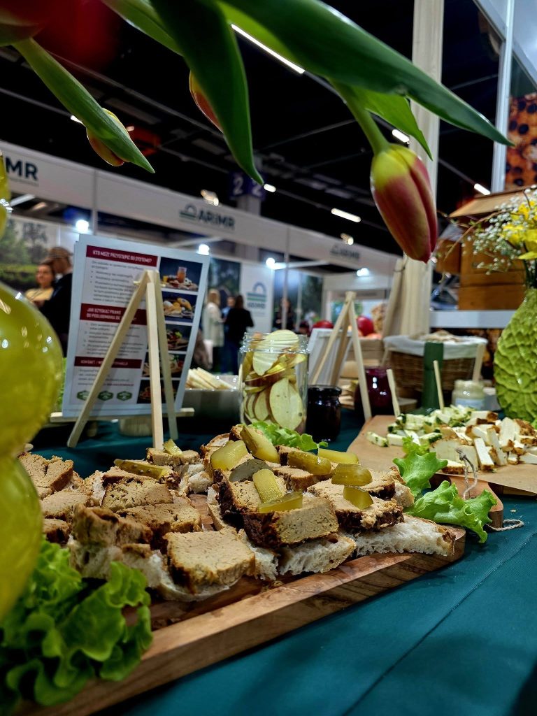 Kanapki z pasztetem i dodatkami podane na drewnianej desce podczas degustacji na stoisku targowym.